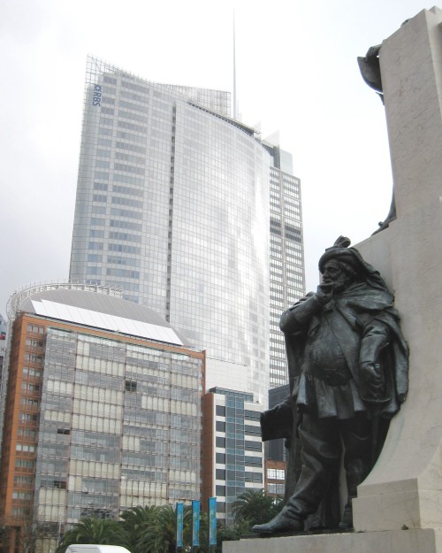 Statue of Falstaff leaning on a stone plinth, skyscrapers in background.
